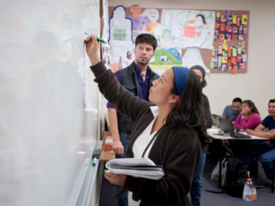 female student writing on a whiteboard with other students looking from their seats